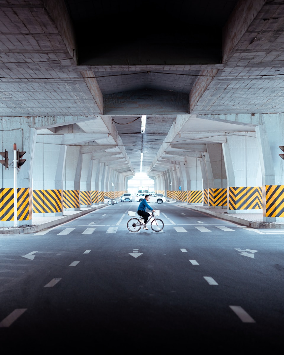 a man riding a bike down a street under a bridge