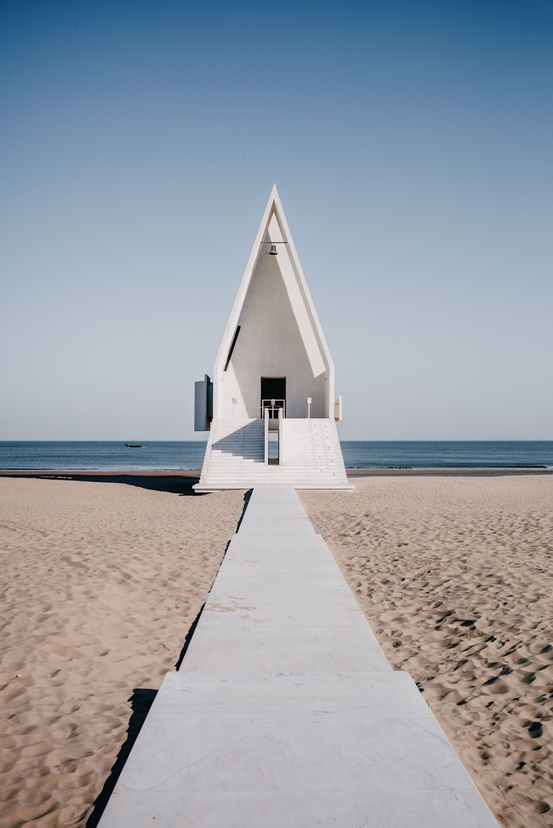 a walkway leading to a white triangular structure on a beach