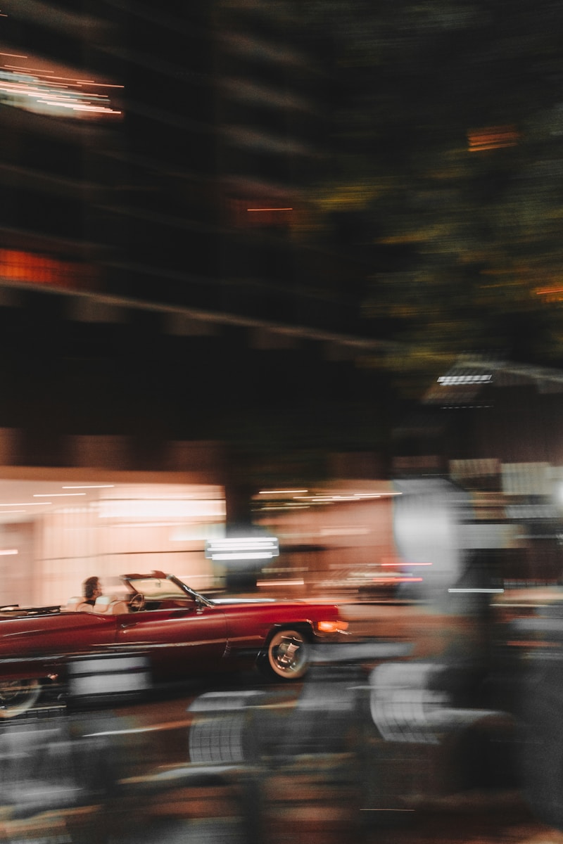 A red car driving down a street next to a tall building